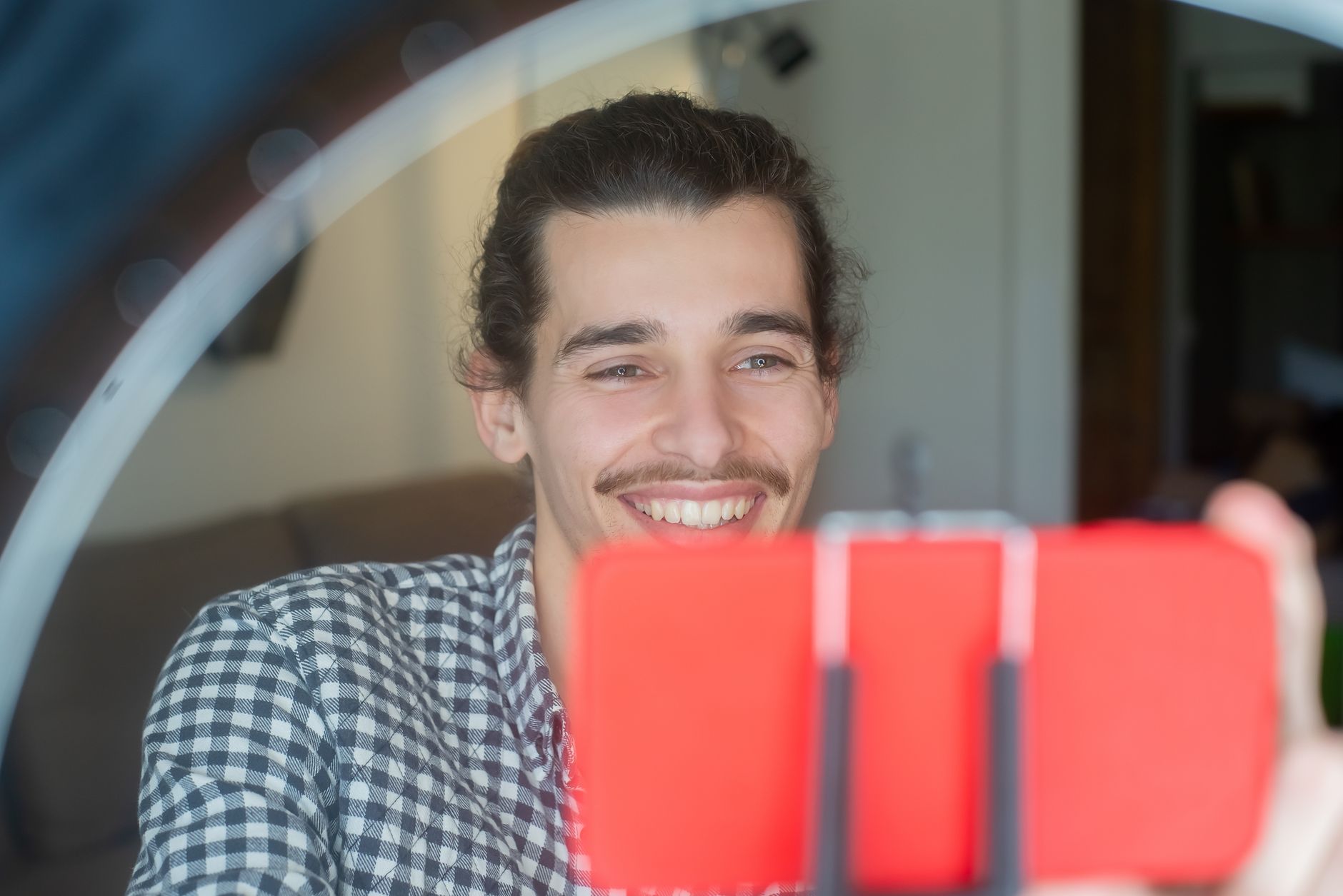 Hombre sonriente ante su móvil, que graba un vídeo, con un aro de luz difuminado al fondo